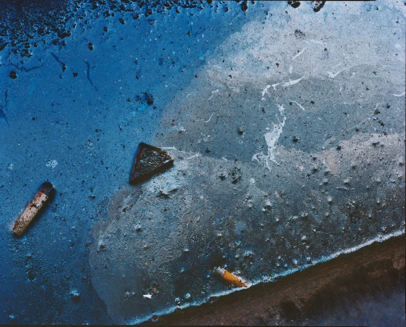 Textured abstract macro shot of dark blue liquid substance with fragments and light gray marble effect, creating an artistic background.