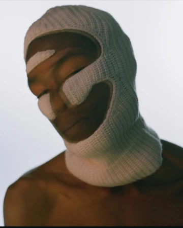 Portrait of a Black man wearing a white crocheted balaclava against a plain white background by Jason Nocito