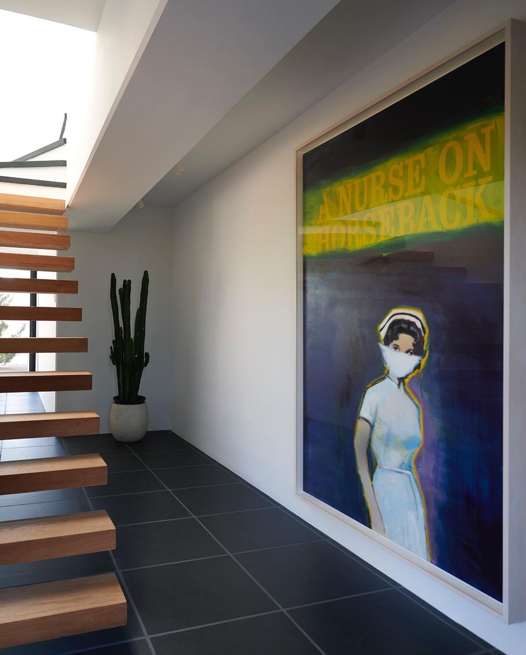 Artwork featuring a nurse in a mask, displayed in a modern interior space with black tile floors and a minimalist wooden staircase.