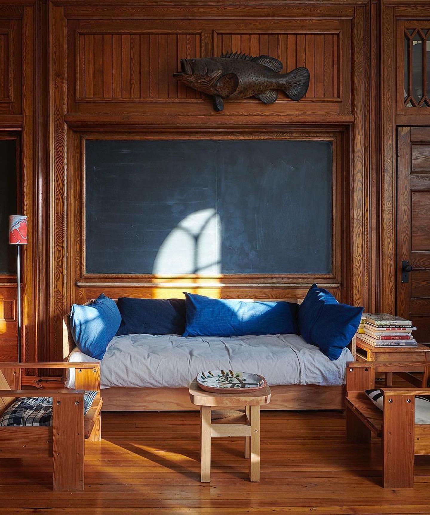Cozy interior features wood-paneled walls, a daybed with blue pillows, and a vintage-style fish decoration above a chalkboard.
