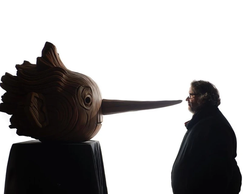 Guillermo del Toro standing next to a large Pinocchio puppet; the figure is silhouetted against a white background, creating a striking profile view.