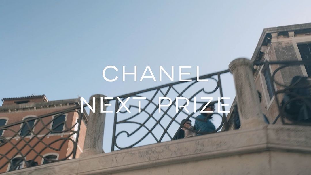 Balcony view of weathered building exterior with architectural detail and 'Chanel Next Prize' text overlay against a pale blue sky.