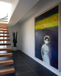 Large framed nurse painting hanging on a white wall in a modern hallway with wooden floating stairs and a potted cactus.