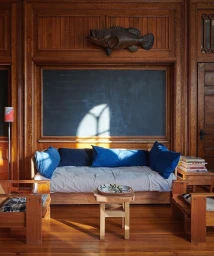 Interior shot featuring a wooden daybed with blue cushions, wood paneled walls, and a mounted fish taxidermy sculpture by Jason Schmidt