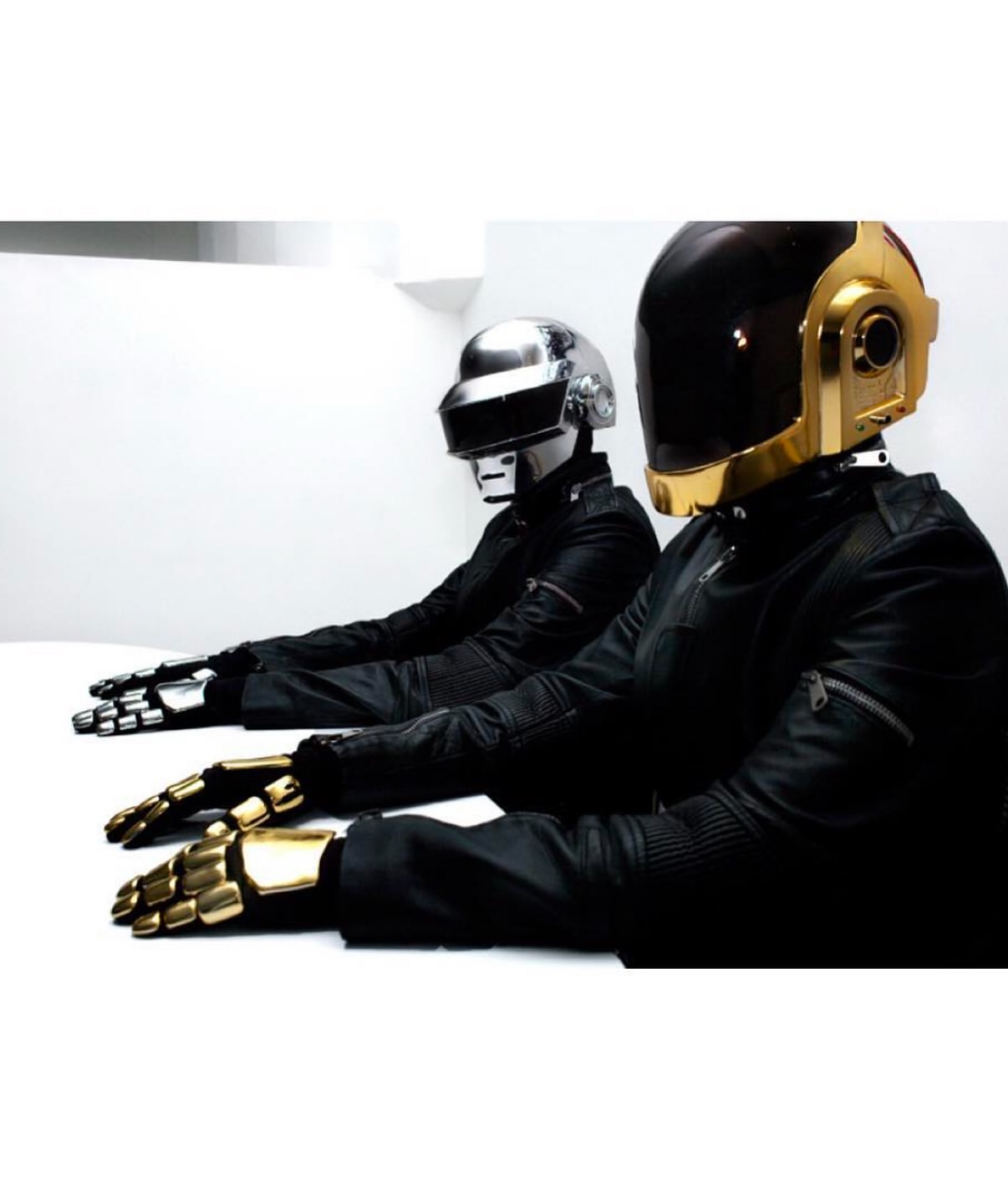 Two people wearing Daft Punk helmets and black jackets sitting at a white table, showcasing music, celebrity and entertainment themes.