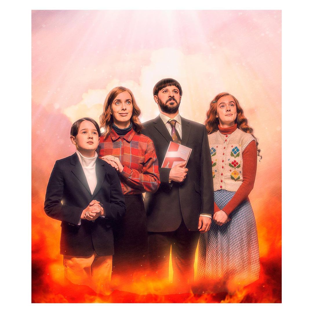 Family of four stands in front of a fiery background, looking upward, bathed in light in a studio photography setting.