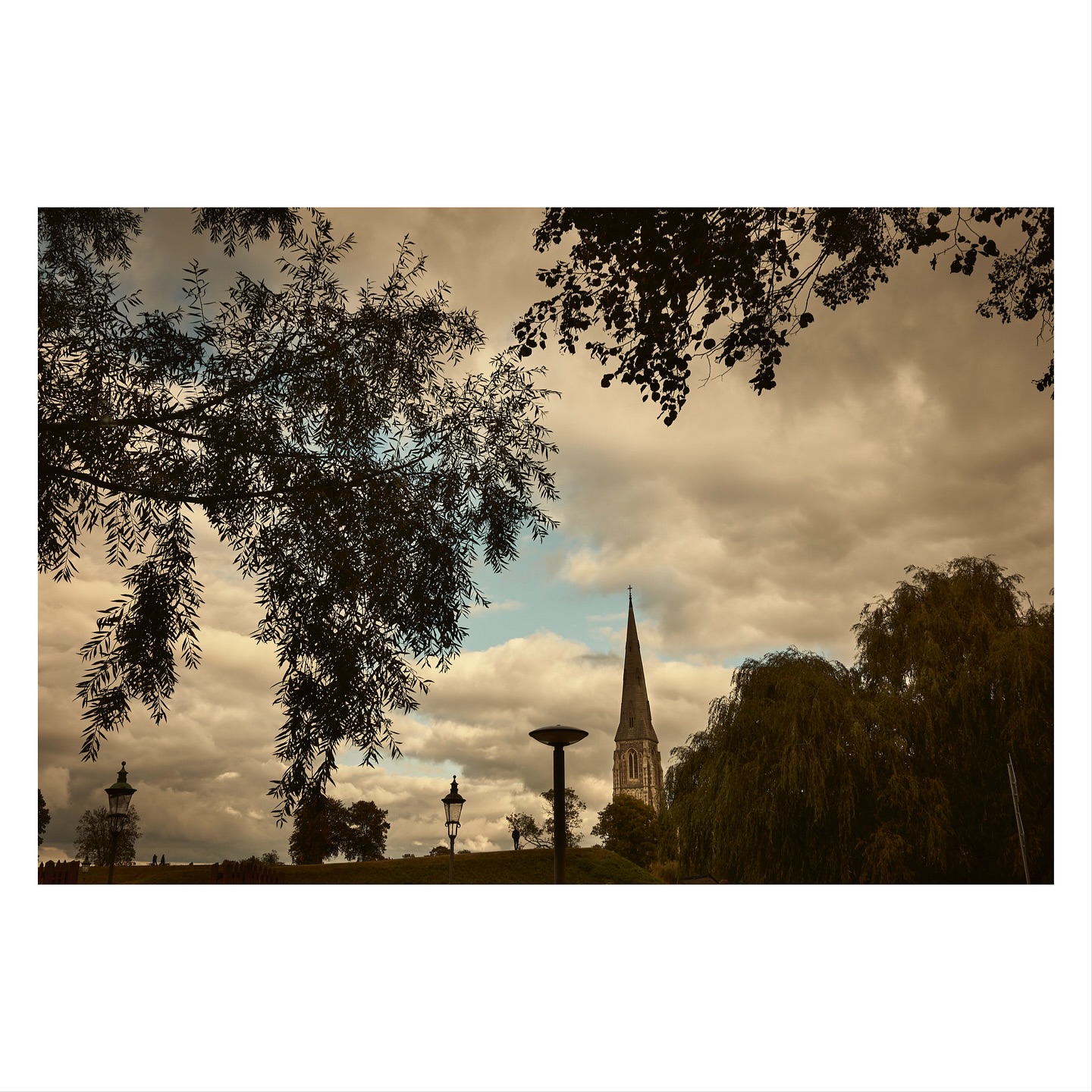 View of St. Alban's Church, Copenhagen, Denmark, framed by silhouetted trees against a cloudy sky, showcasing architectural detail and serene atmosphere.