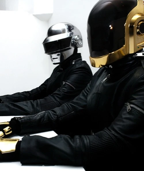 Two musicians wearing black leather jackets and helmets sit at a table, in a music studio. One helmet is silver, the other is gold.