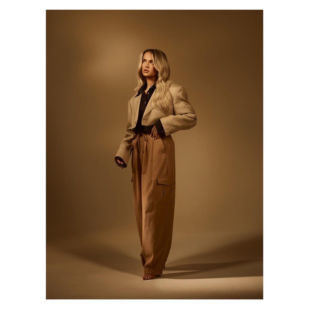 Woman in beige blazer and tan pants posing in a studio with soft lighting, fashion portrait. The model is looking up and to the left.