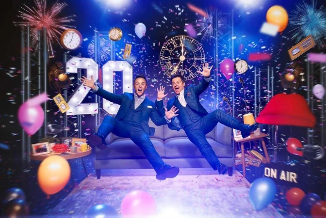 Two men in suits jumping against a backdrop of clocks, balloons, and confetti, creating a festive and energetic atmosphere for an event.