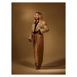 Blonde woman wearing beige cropped jacket and cargo pants standing against a warm brown seamless backdrop