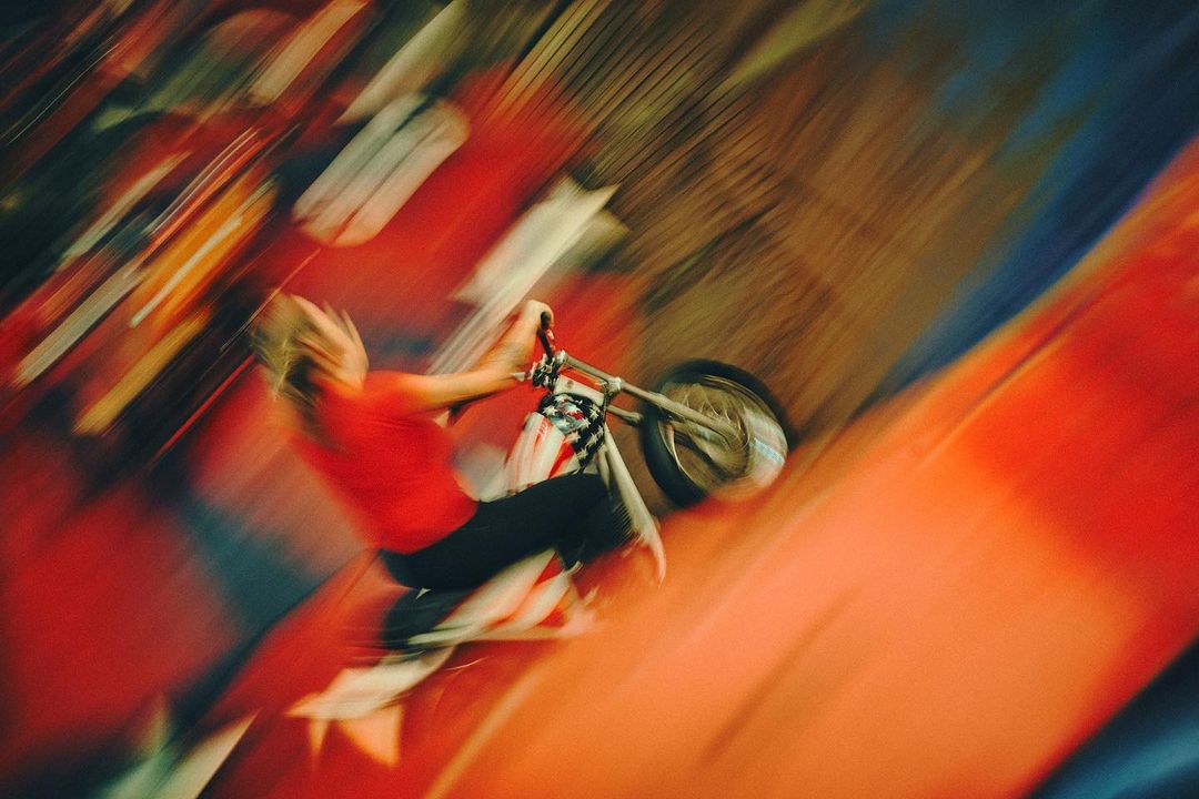 Adult on a motorbike with long exposure and motion blur against a red background in an abstract outdoor shot.