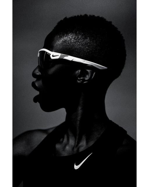 Profile shot of a dark-skinned adult wearing sunglasses and a tank top with a Nike logo against a dark grey gradient background.