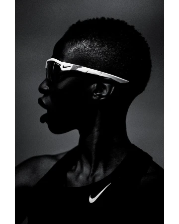 Profile shot of a dark-skinned adult wearing sunglasses and a tank top with a Nike logo against a dark grey gradient background.