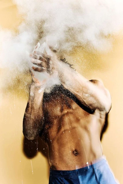 Muscular man clapping hands in a studio setting, creating a cloud of white powder dust, showcasing fitness and raw energy.