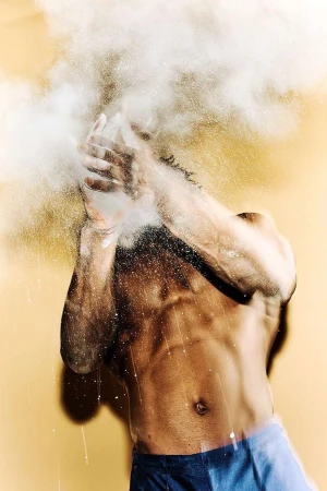 Muscular man clapping hands in a studio setting, creating a cloud of white powder dust, showcasing fitness and raw energy.