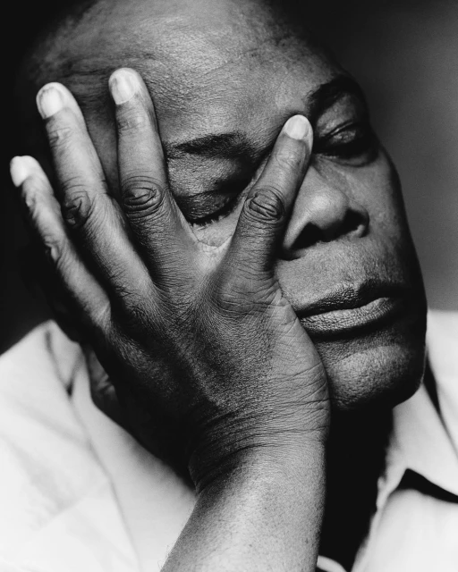 Monochrome portrait of an African American man with his face partially covered by his hand, eyes closed, capturing a pensive mood.