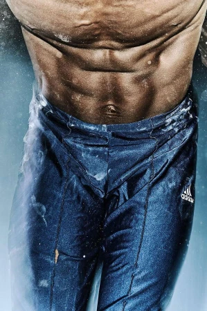 Close-up of the torso of a muscular man, showing his abs and waist with blue athletic pants, dust particles in the air. 