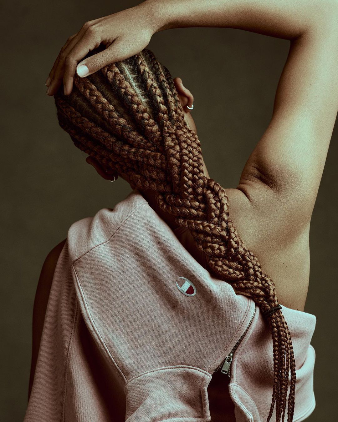 Woman with braided hair and light pink Champion sweatshirt poses in a studio. Back view, fashion, beauty, hair and clothing.