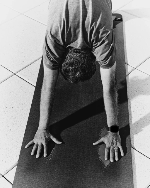 Monochrome shot of an adult doing a downward-facing dog yoga pose on a mat indoors, wearing an activity tracker.