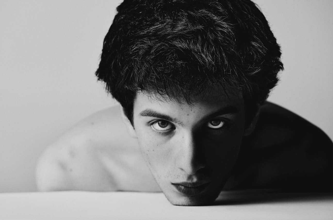 Close-up monochrome portrait of a young man leaning forward against a plain white background by photographer Jay Kolsch.