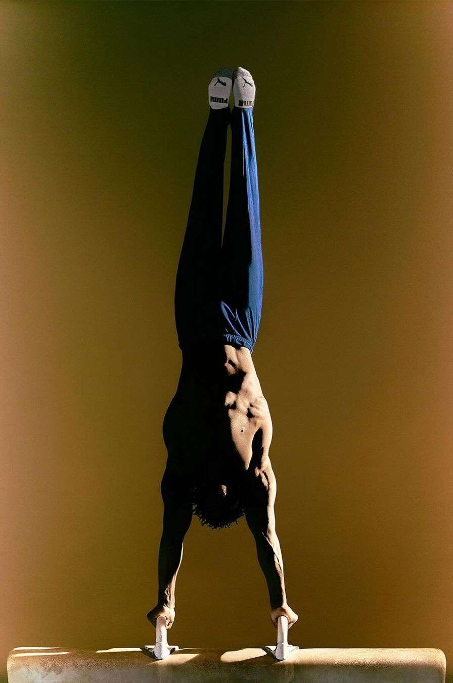 Gymnast performs handstand on pommel horse, showcasing strength and balance in a brightly lit setting.