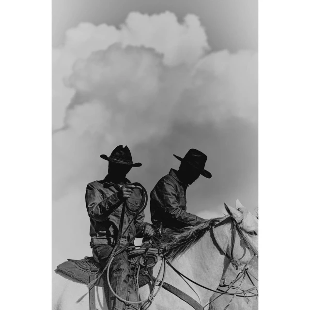 Two cowboys on horseback under a cloudy sky in black and white. They wear hats, jackets and one holds a rope, capturing an old west aesthetic.