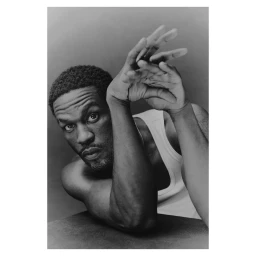 Monochrome portrait of a Black man with short textured hair wearing a white tank top, holding hands up near his face