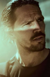 Close-up portrait of a man with dark hair, a beard, and a t-shirt, lit by a strong side light by photographer Jay Kolsch.