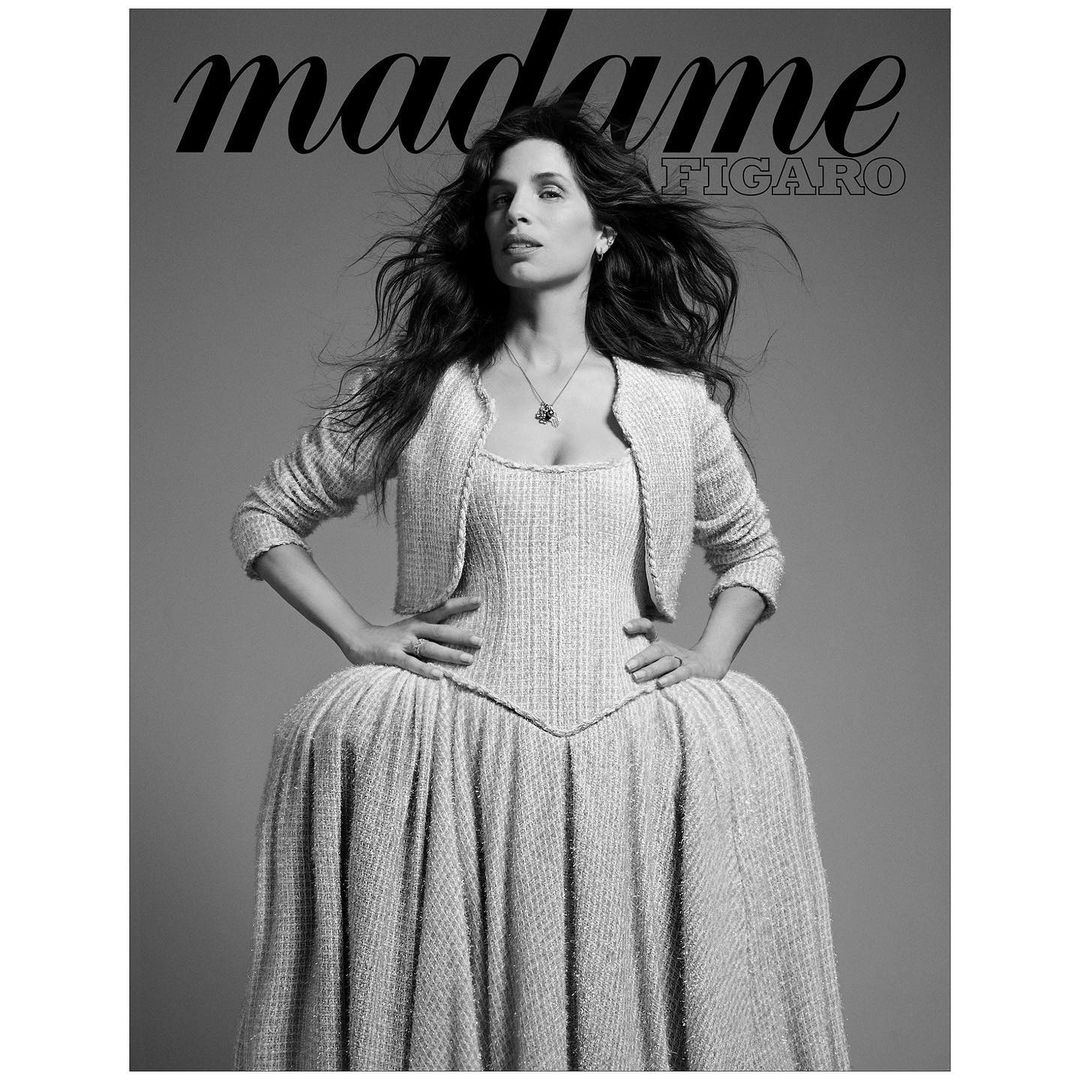 Black and white portrait of a woman in a formal dress and cropped jacket, posing with hands on her waist for a magazine cover.