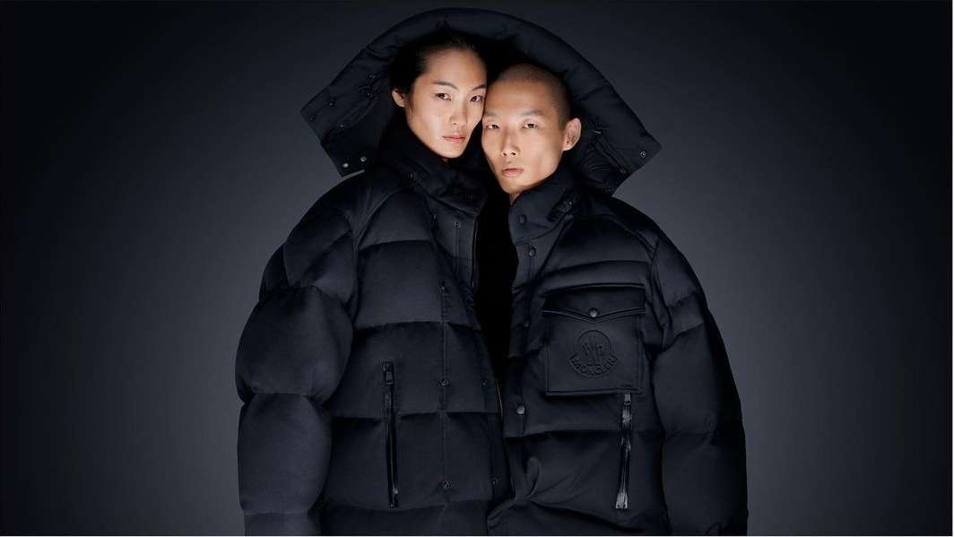 A stylish portrait features an Asian couple in hooded black puffer jackets against a dark backdrop, exuding a modern, fashionable aesthetic.