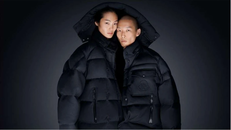 A stylish portrait features an Asian couple in hooded black puffer jackets against a dark backdrop, exuding a modern, fashionable aesthetic.