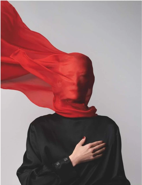 Abstract portrait of a person covered in a flowing red scarf, set against a neutral background, wearing a black shirt.