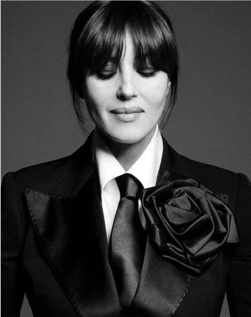Black and white portrait of woman with dark hair and bangs wearing a suit with a flower detail on the lapel. Eyes closed.