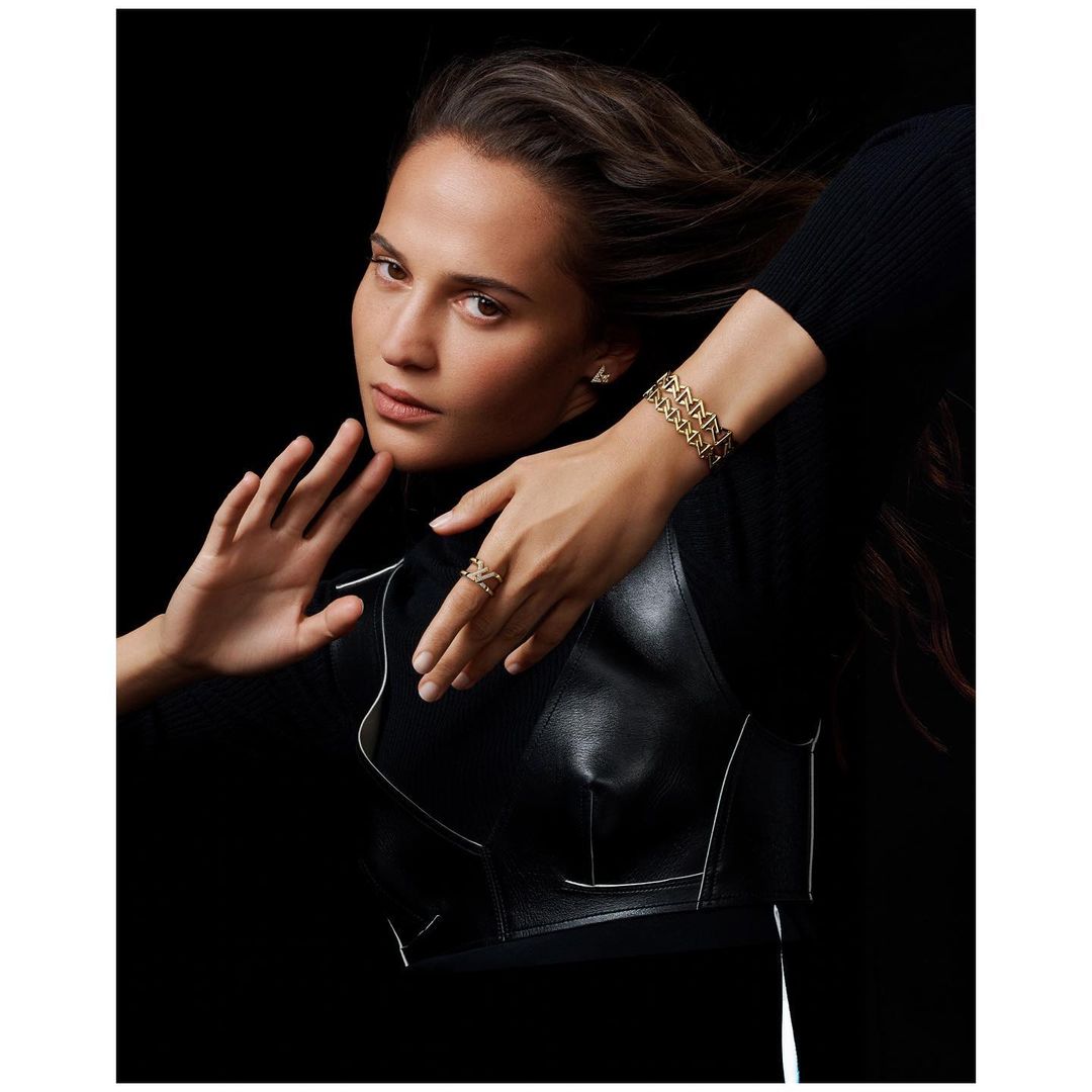 Attractive adult female wearing designer gold jewelry in a studio shot with a black background and leather vest.