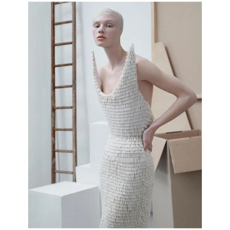 Model in a white fringed dress wearing a fitted head cap posing in a studio with props.