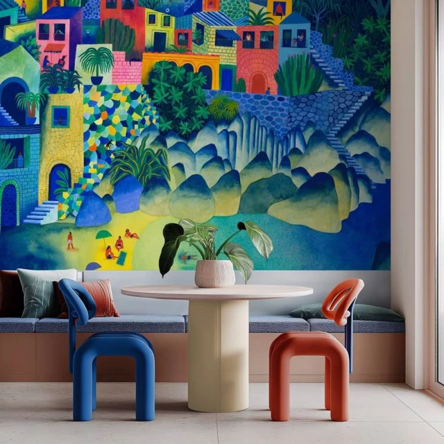 Indoor scene with colorful illustration of a coastal village, set against blue and green hills, with table and chairs in foreground.
