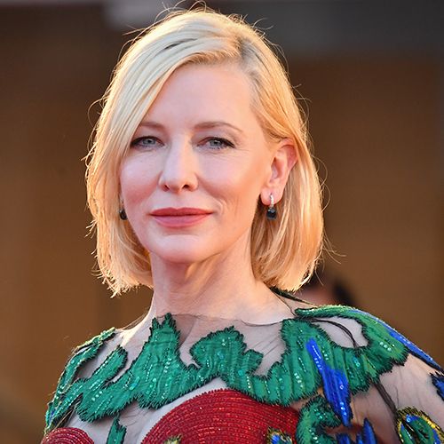 Close-up portrait of Cate Blanchett with blonde bob hairstyle, wearing a green and red embellished dress and small drop earrings.