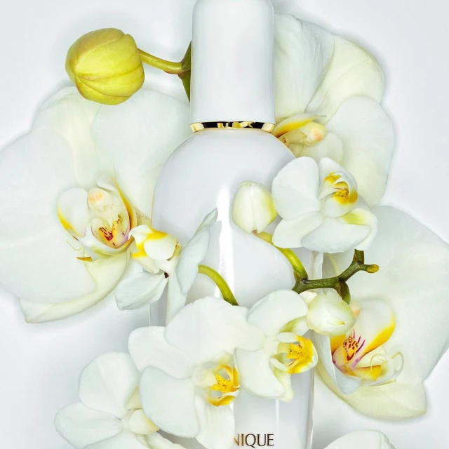 White skincare bottle surrounded by white orchid flowers, shot in a photo studio setting with bright lighting and soft shadows.