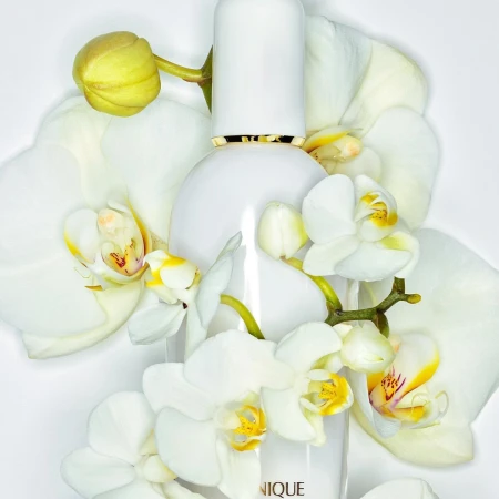 White skincare bottle surrounded by white orchid flowers, shot in a photo studio setting with bright lighting and soft shadows.
