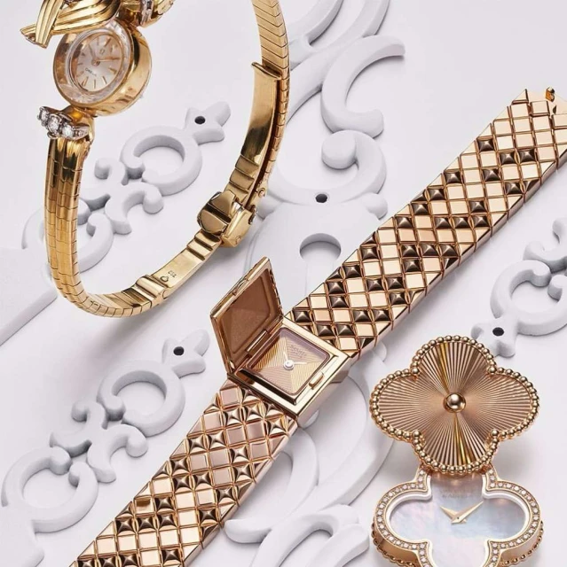 Three gold vintage wristwatches, each with unique bracelet designs, are elegantly arranged on a white surface with decorative flourishes.