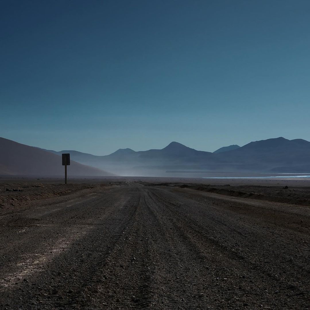 Distant mountains and a vast, empty landscape are visible under a clear blue sky, creating a sense of solitude and open space.