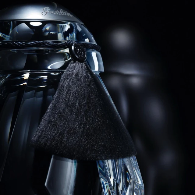 Crystal Guerlain perfume bottle with a black tassel on a dark background, product shot for beauty and fashion industries.
