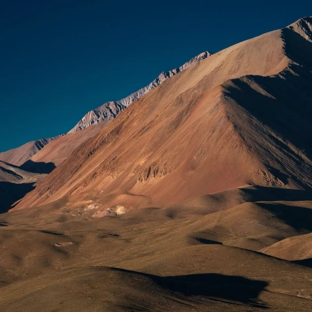 Striking landscape photograph captures a vast, mountainous desert terrain under a clear blue sky, showcasing the rugged beauty of nature.