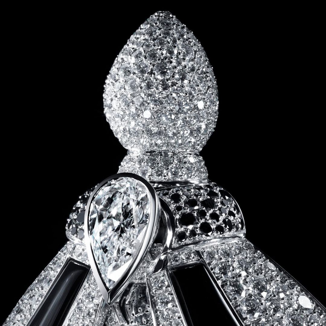 Close-up of an ornate jewelry object featuring many small diamonds and one large pear-shaped diamond, set against a stark black background.