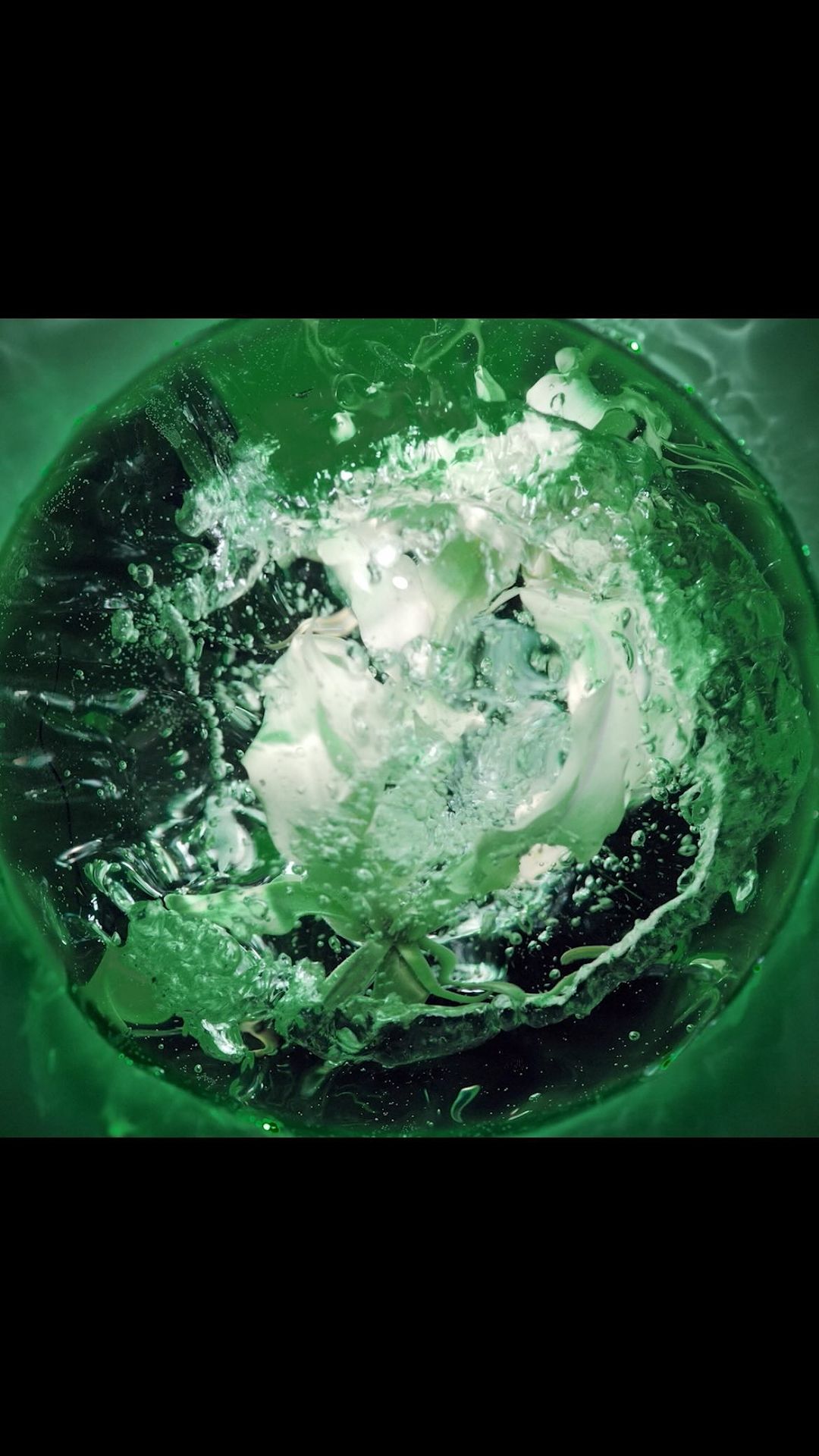 Underwater shot of a translucent sphere with green tint, water, and bubbles inside, captured with dramatic lighting.
