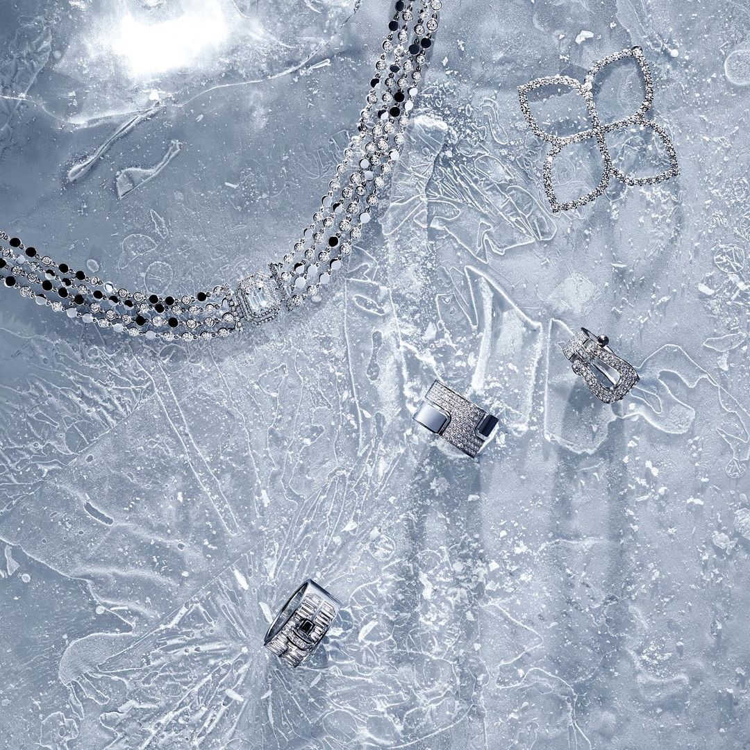 Overhead shot of a sparkling diamond necklace, ring, flower shaped earrings, and stud earrings displayed on a textured gray surface.