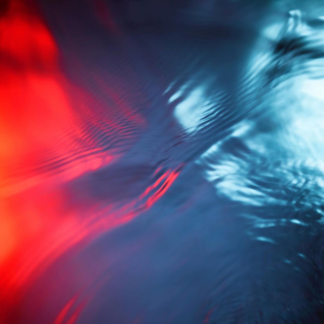 Abstract ripples of water illuminated by contrasting red and blue light creating dynamic fluid texture.