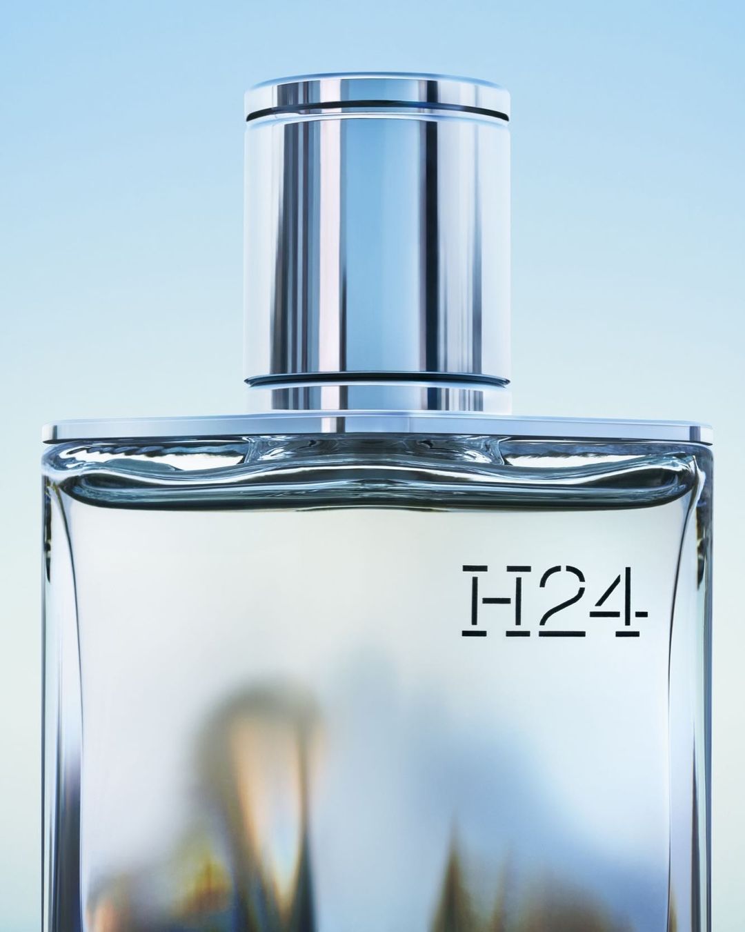 Elegant studio shot of H24 fragrance bottle with silver cap against a soft blue background, showcasing its design and minimalist aesthetic.
