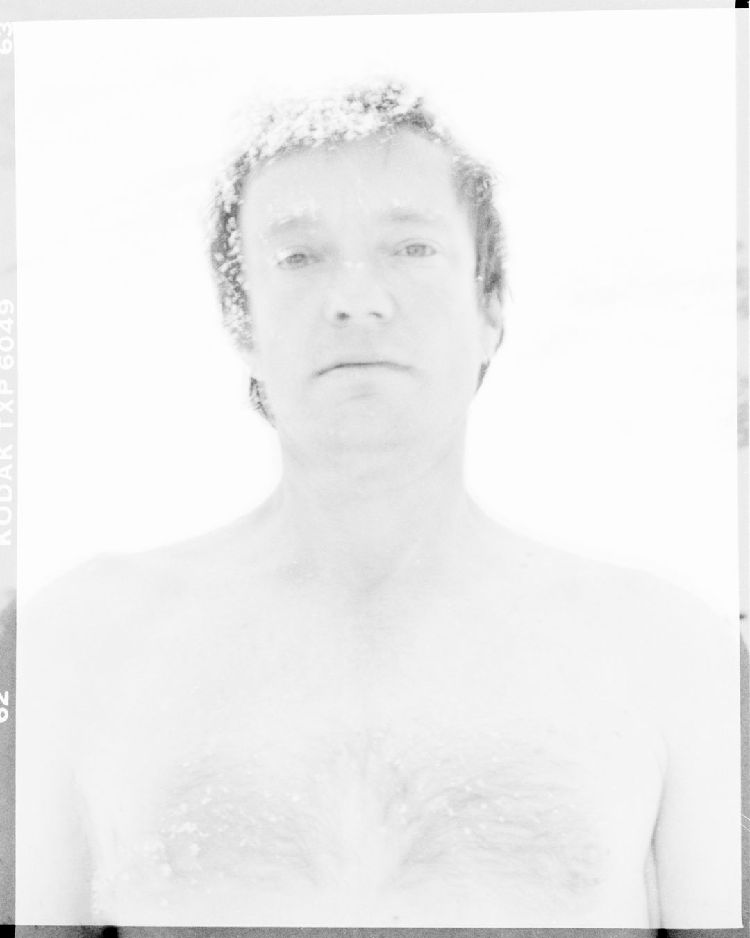 Monochrome portrait of an adult male with short hair, fair skin, and a slight smile against a bright white background.